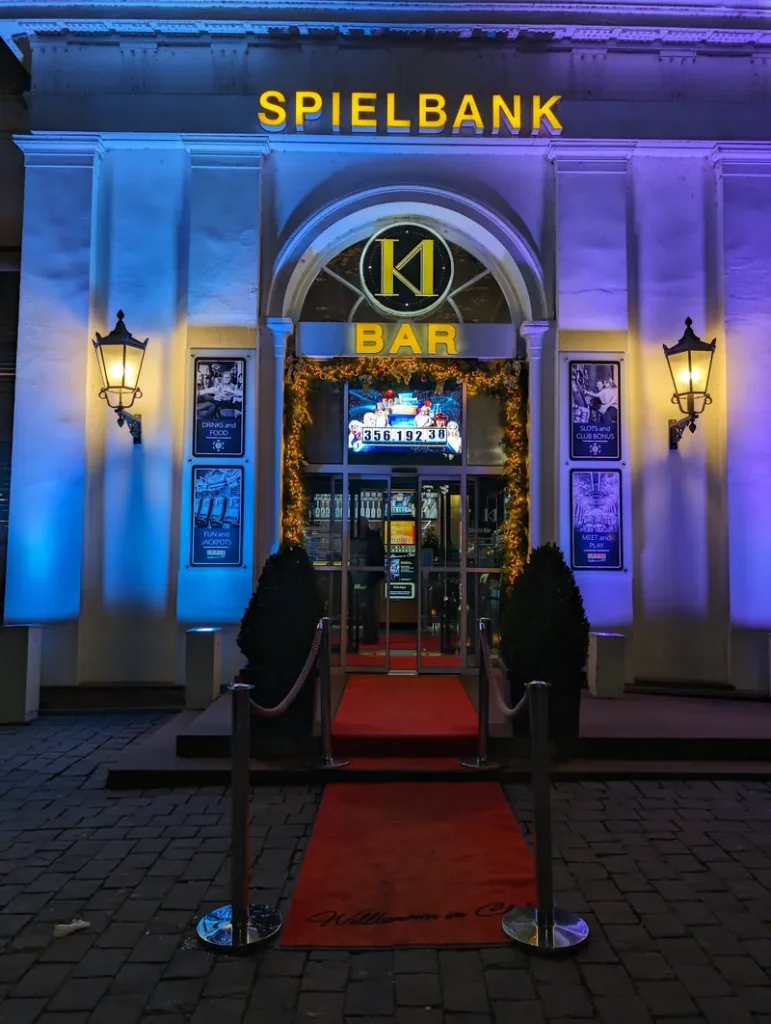 Beleuchteter Eingang zur Spielbank Wiesbaden bei Nacht mit blauem Licht, rotem Teppich und „Bar“-Schild