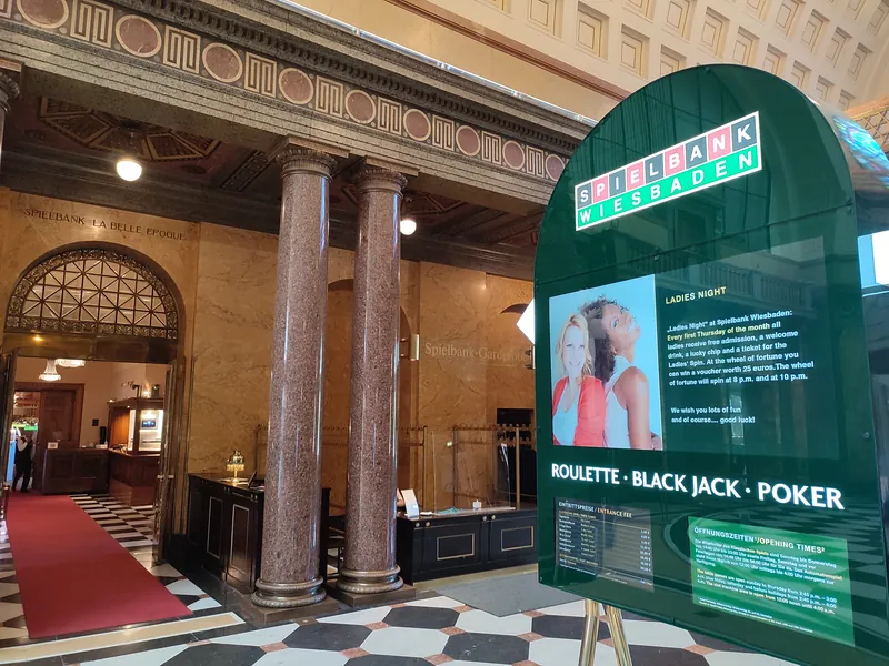 Foyer der Spielbank Wiesbaden mit Marmorsäulen, Registrierungstheke und einem Schild für die „Ladies Night“