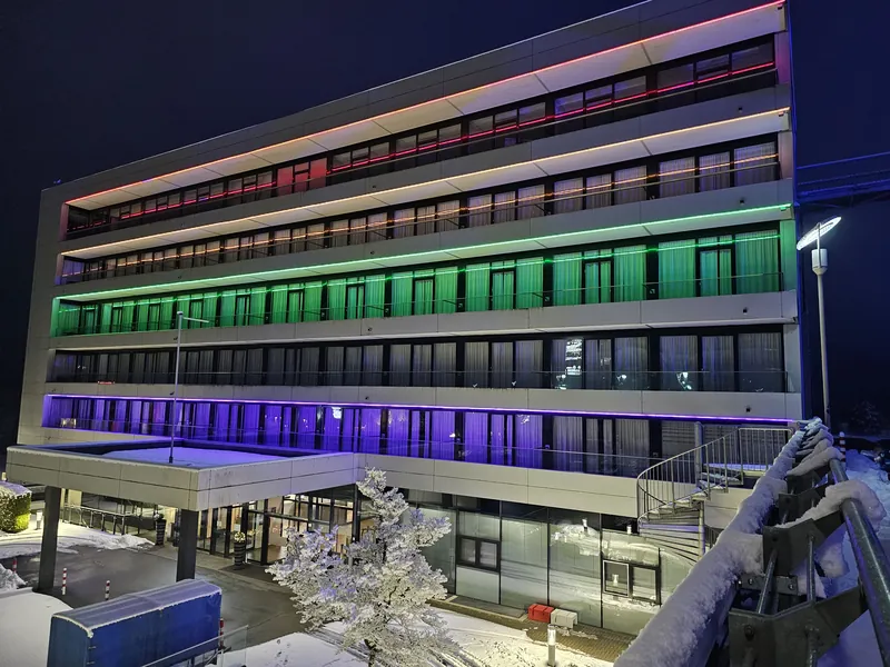 Nachtaufnahme des Ring Casino Gebäudes, beleuchtet mit farbigen LED-Lichtbändern und Schnee auf dem Boden